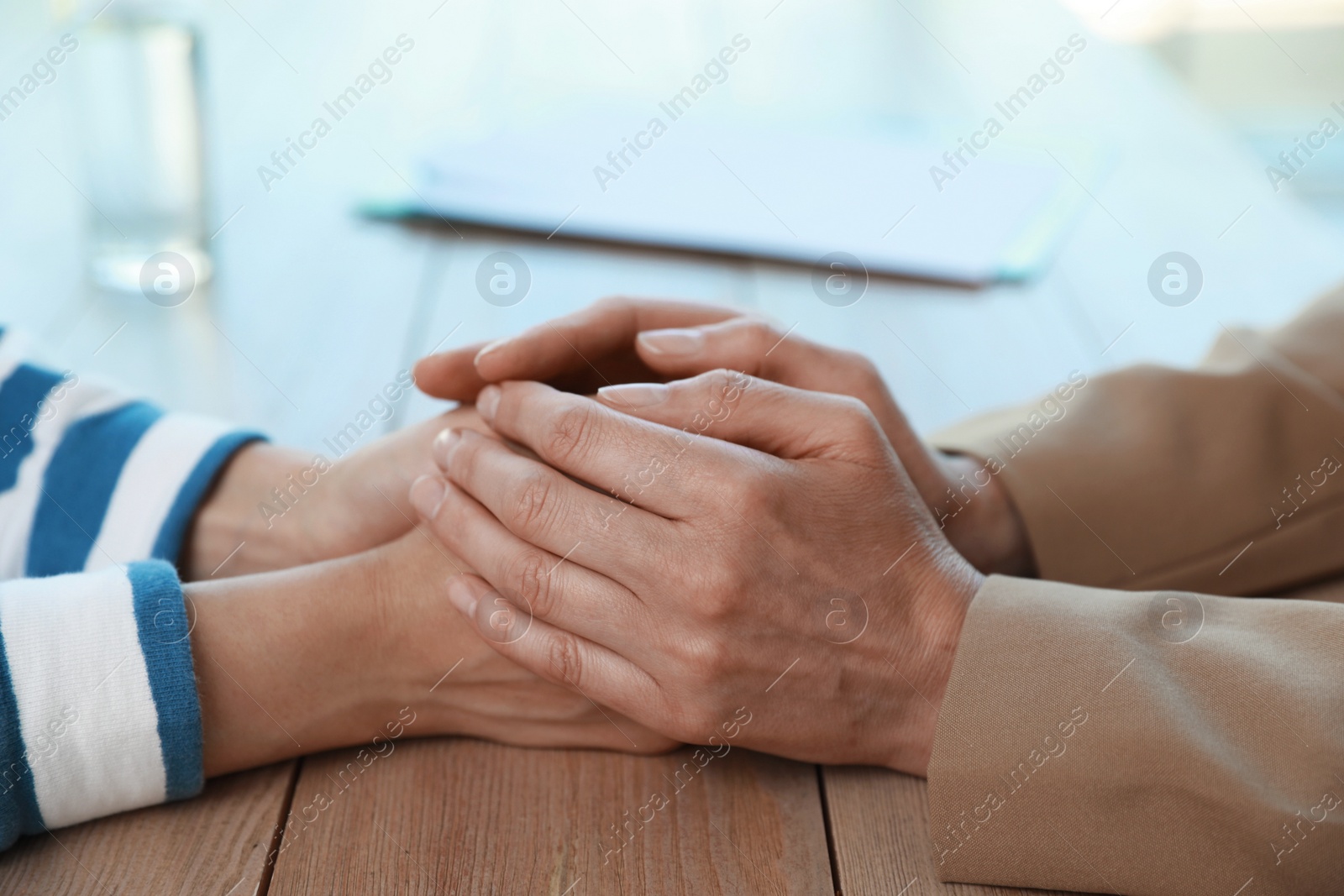 Photo of Psychotherapist holding patient's hands at table indoors, closeup