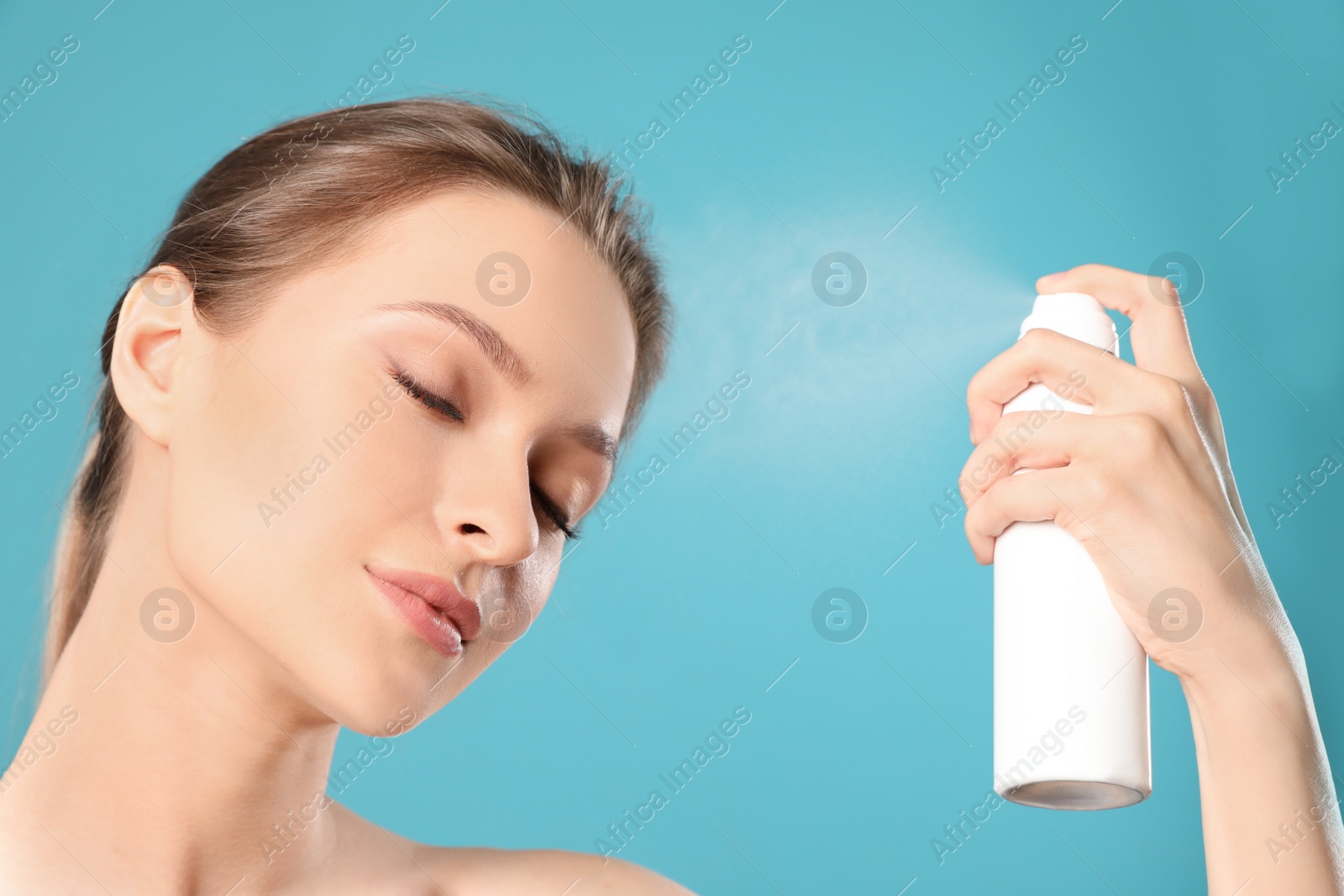 Photo of Young woman applying thermal water on face against color background. Cosmetic product