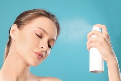 Young woman applying thermal water on face against color background. Cosmetic product