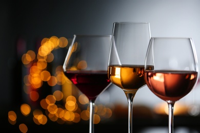 Photo of Glasses with different wines against defocused lights, closeup. Space for text