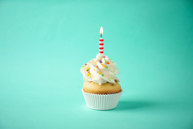Delicious birthday cupcake with candle on light green background