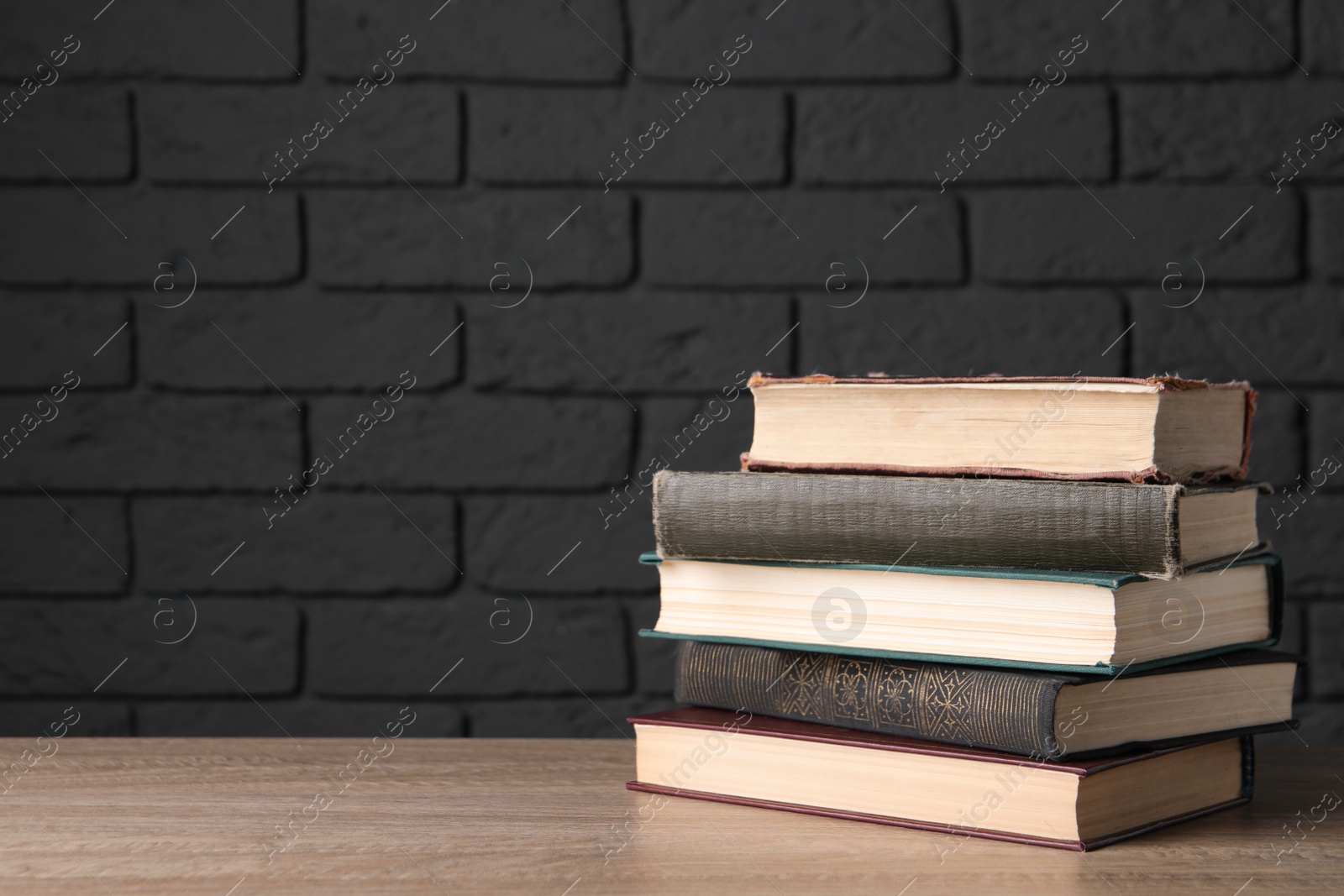 Photo of Stack of old hardcover books on wooden table near black brick wall, space for text