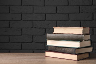 Photo of Stack of old hardcover books on wooden table near black brick wall, space for text