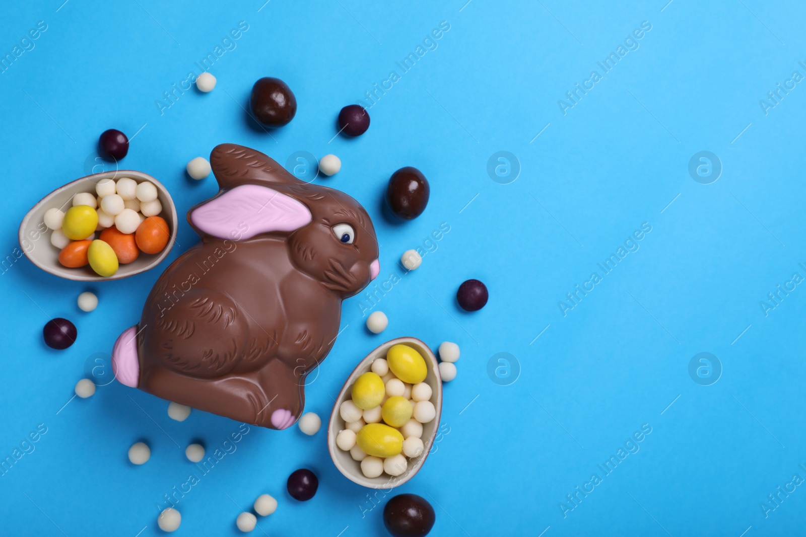 Photo of Chocolate Easter bunny, halves of egg and candies on light blue background, flat lay. Space for text