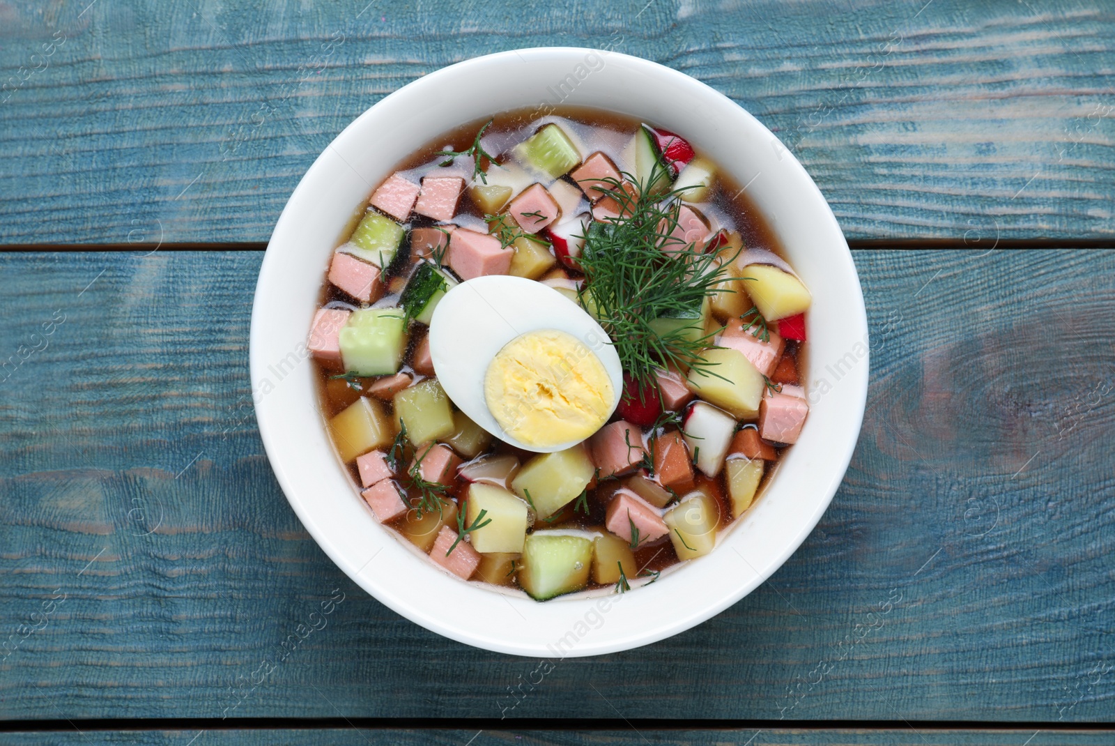 Photo of Delicious cold okroshka with kvass on blue wooden table, top view. Traditional Russian summer soup