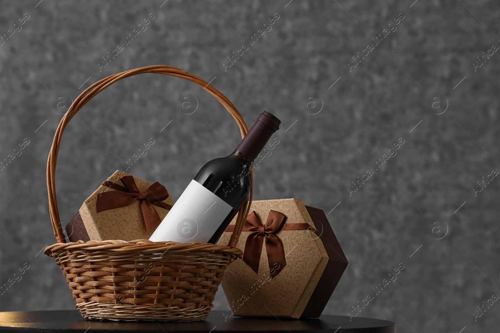 Photo of Wicker basket with bottle of wine and gift boxes on table. Space for design