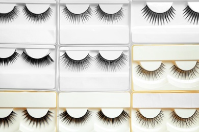 Set with different false eyelashes in packs as background, top view