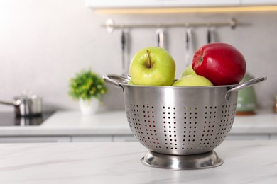 Photo of Colander with fresh apples on white marble table in kitchen. Space for text