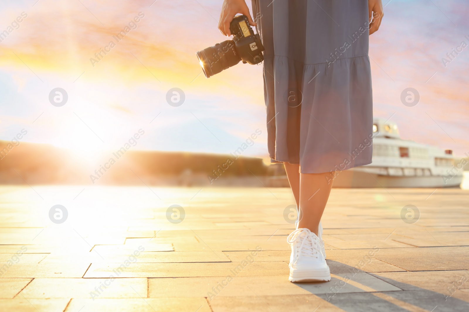 Photo of Young female photographer with professional camera in sunset lights at pier. Space for text