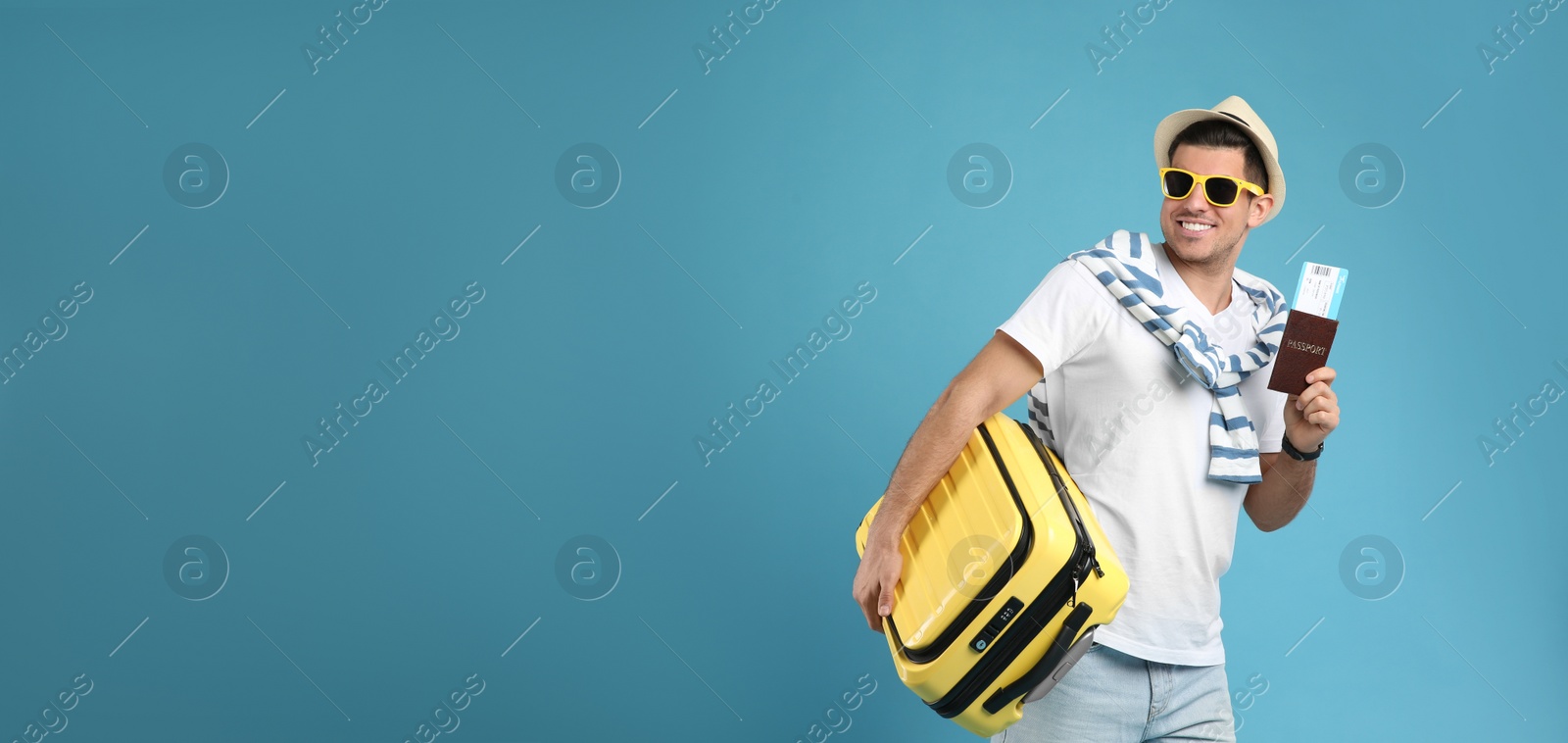 Photo of Male tourist holding passport with ticket and suitcase on turquoise background