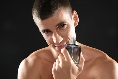 Handsome young man with bottle of perfume on black background