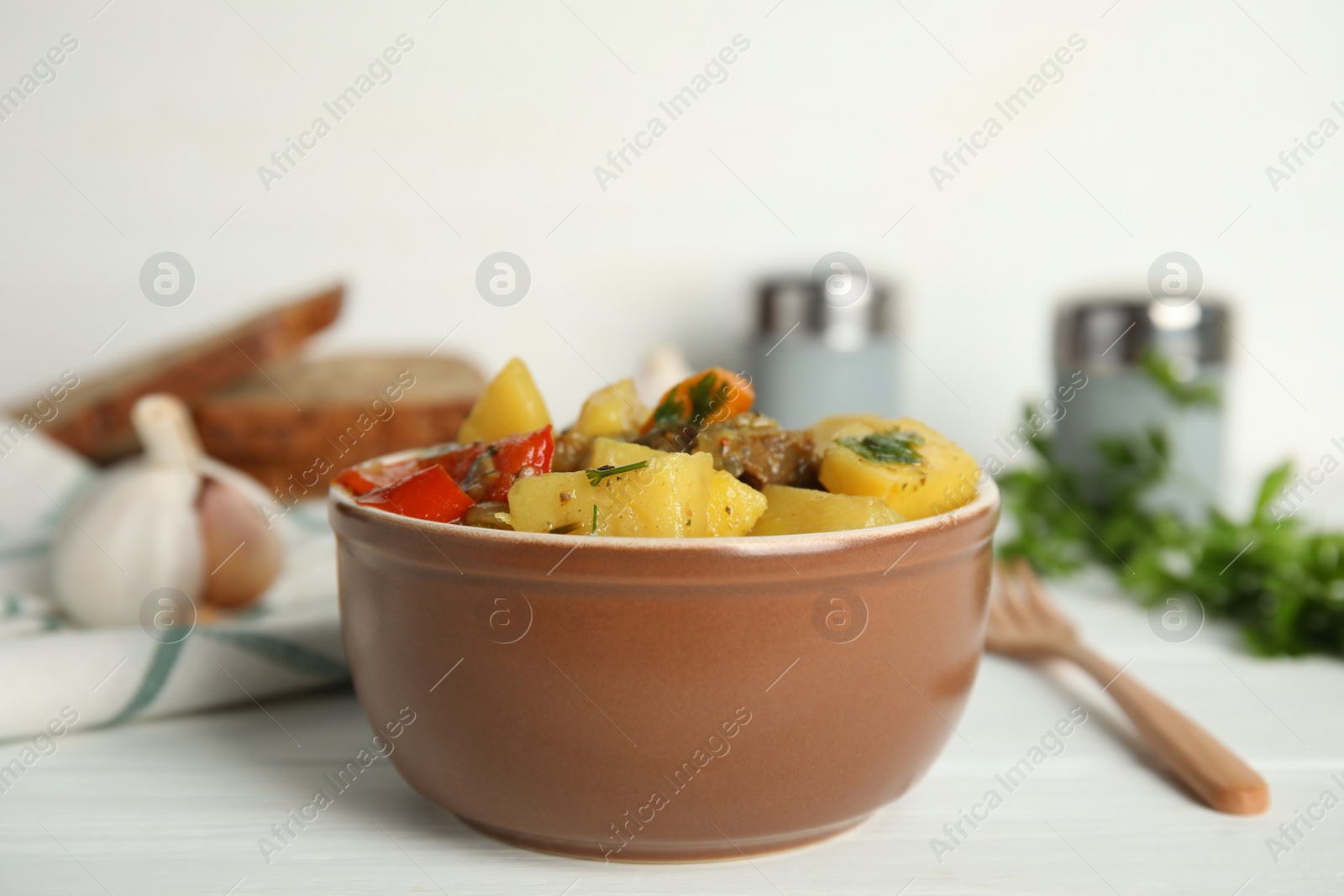 Photo of Tasty cooked dish with potatoes in earthenware served on white wooden table