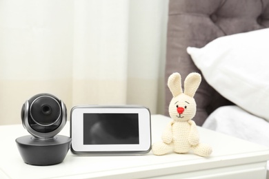 Photo of Baby monitor with camera and toy on table in bedroom. Video nanny
