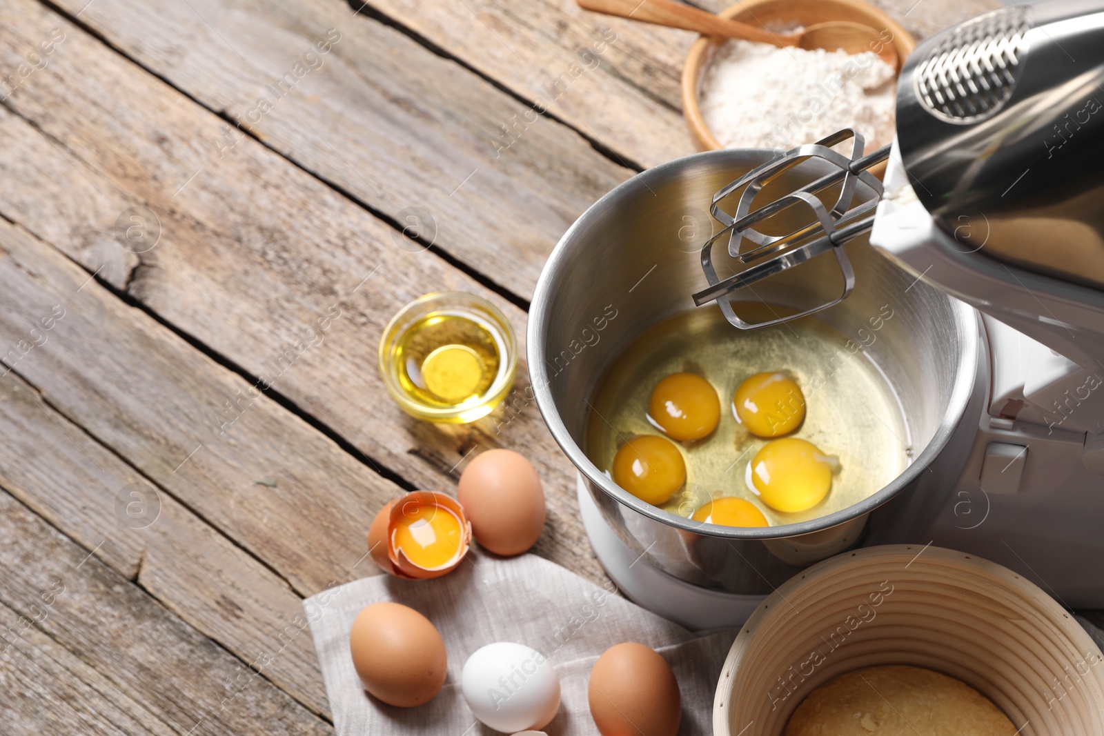 Photo of Making dough. Raw eggs in bowl of stand mixer and ingredients on wooden table, space for text