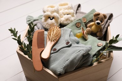 Photo of Wooden crate with children's clothes, shoes, toy, pacifier, hair brush and comb on white table