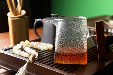 Pitcher with freshly brewed pu-erh tea and prayer beads on wooden tray, closeup
