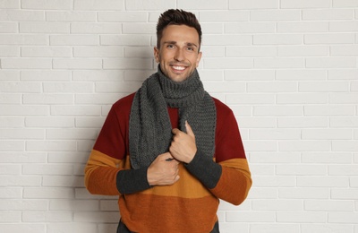 Photo of Happy young man in scarf and warm sweater near white brick wall. Winter season