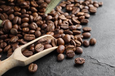 Photo of Wooden scoop with roasted coffee beans on black table, closeup