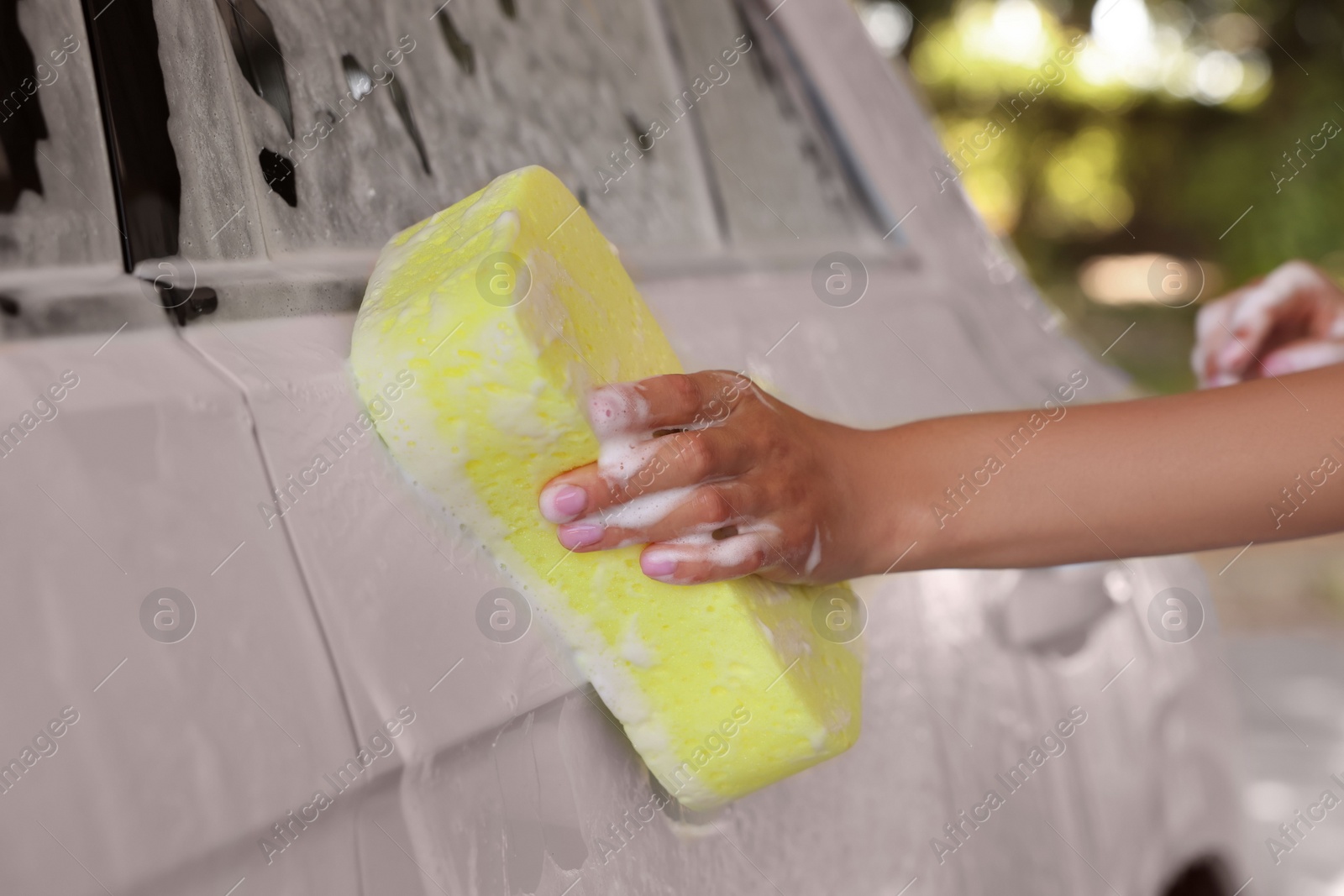 Photo of Woman washing car with sponge outdoors, closeup