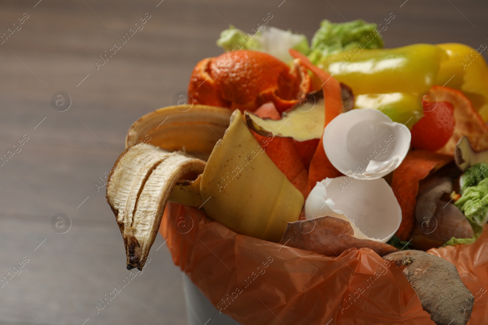 Photo of Trash bin with organic waste for composting on wooden background, closeup