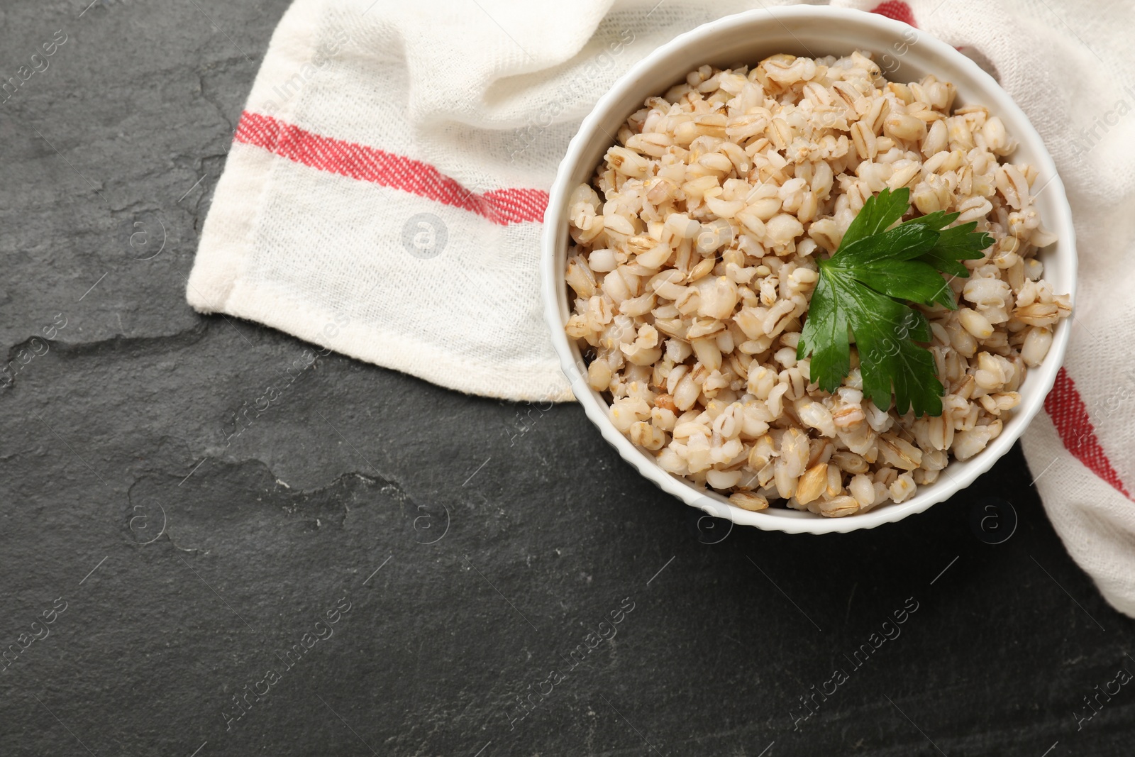 Photo of Tasty pearl barley porridge in bowl on dark textured table, top view. Space for text