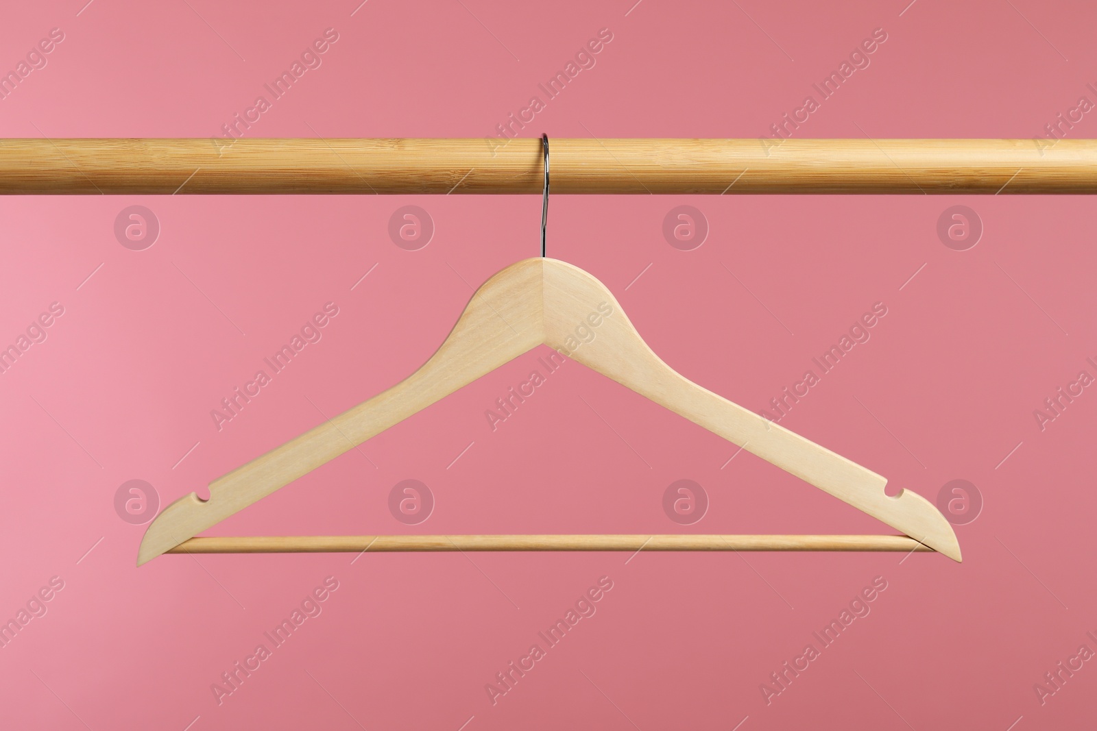 Photo of Empty clothes hanger on wooden rack against pink background