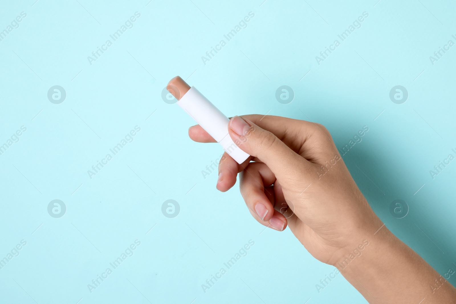 Photo of Woman holding hygienic lipstick on turquoise background, closeup