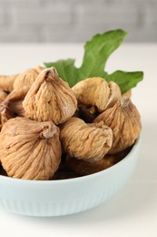 Bowl with tasty dried figs and green leaf on white wooden table, closeup