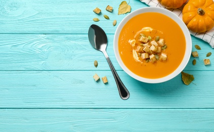 Photo of Tasty creamy pumpkin soup with croutons and seeds in bowl on light blue wooden table, flat lay. Space for text