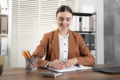 Photo of Happy woman taking notes at wooden table in office