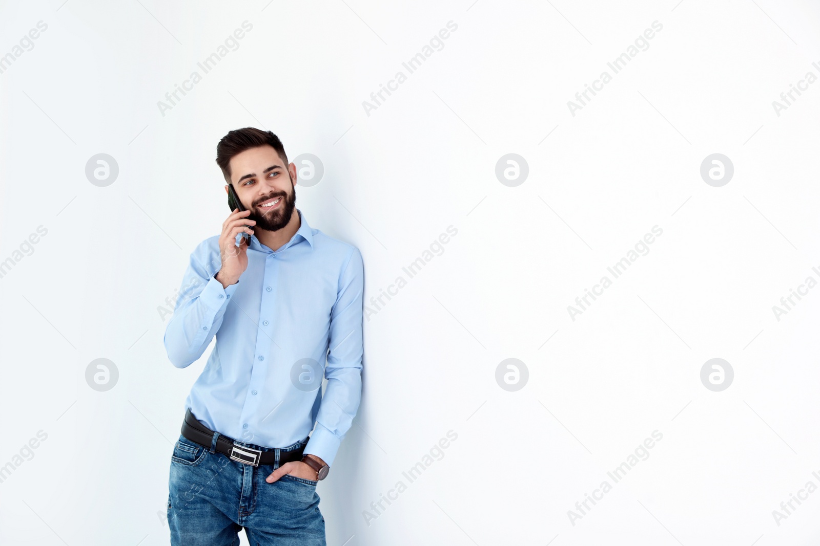 Photo of Handsome young man talking with client by phone near white wall, space for text. Working time