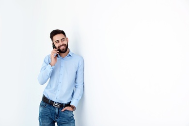 Handsome young man talking with client by phone near white wall, space for text. Working time