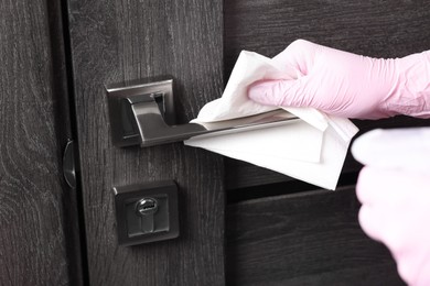 Photo of Woman wiping door handle with paper towel, closeup