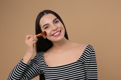 Photo of Happy woman applying makeup on light brown background