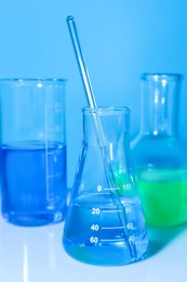 Glass flasks with colorful liquids on white table against light blue background