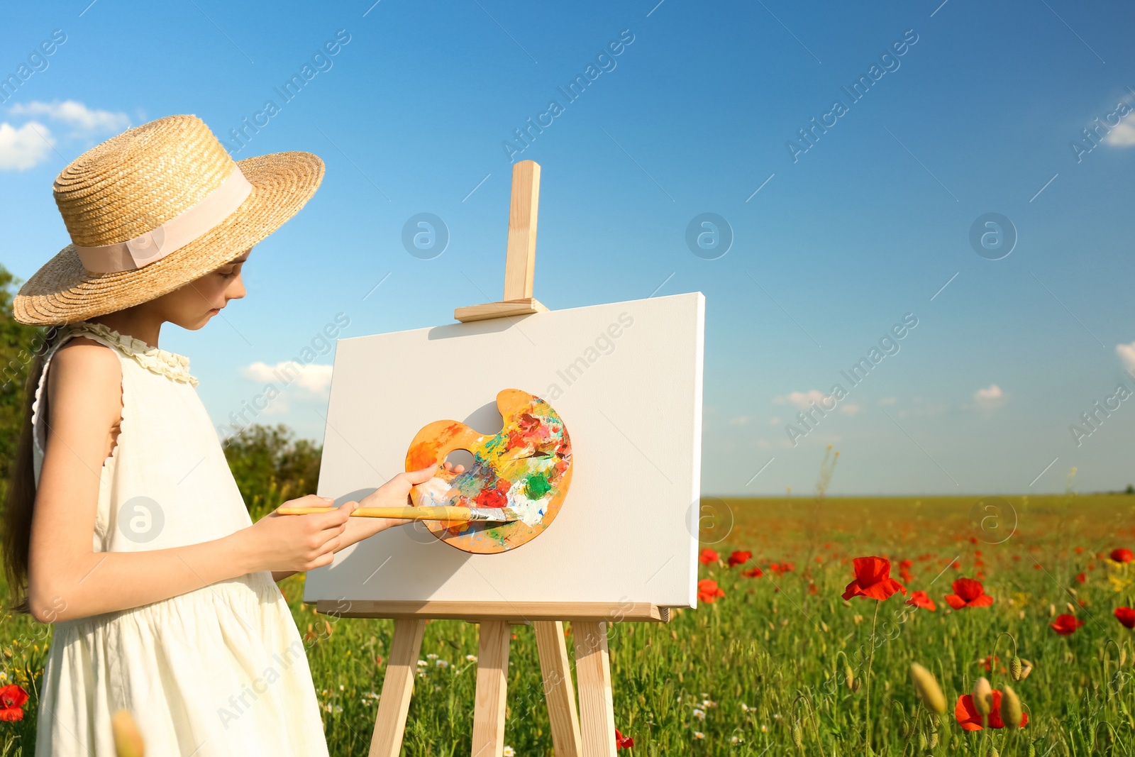 Photo of Little girl painting on easel in beautiful poppy field