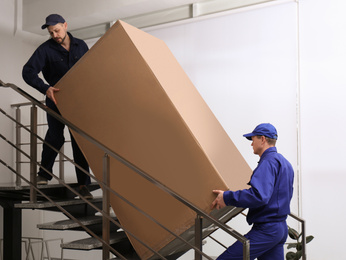 Professional workers carrying refrigerator on stairs indoors