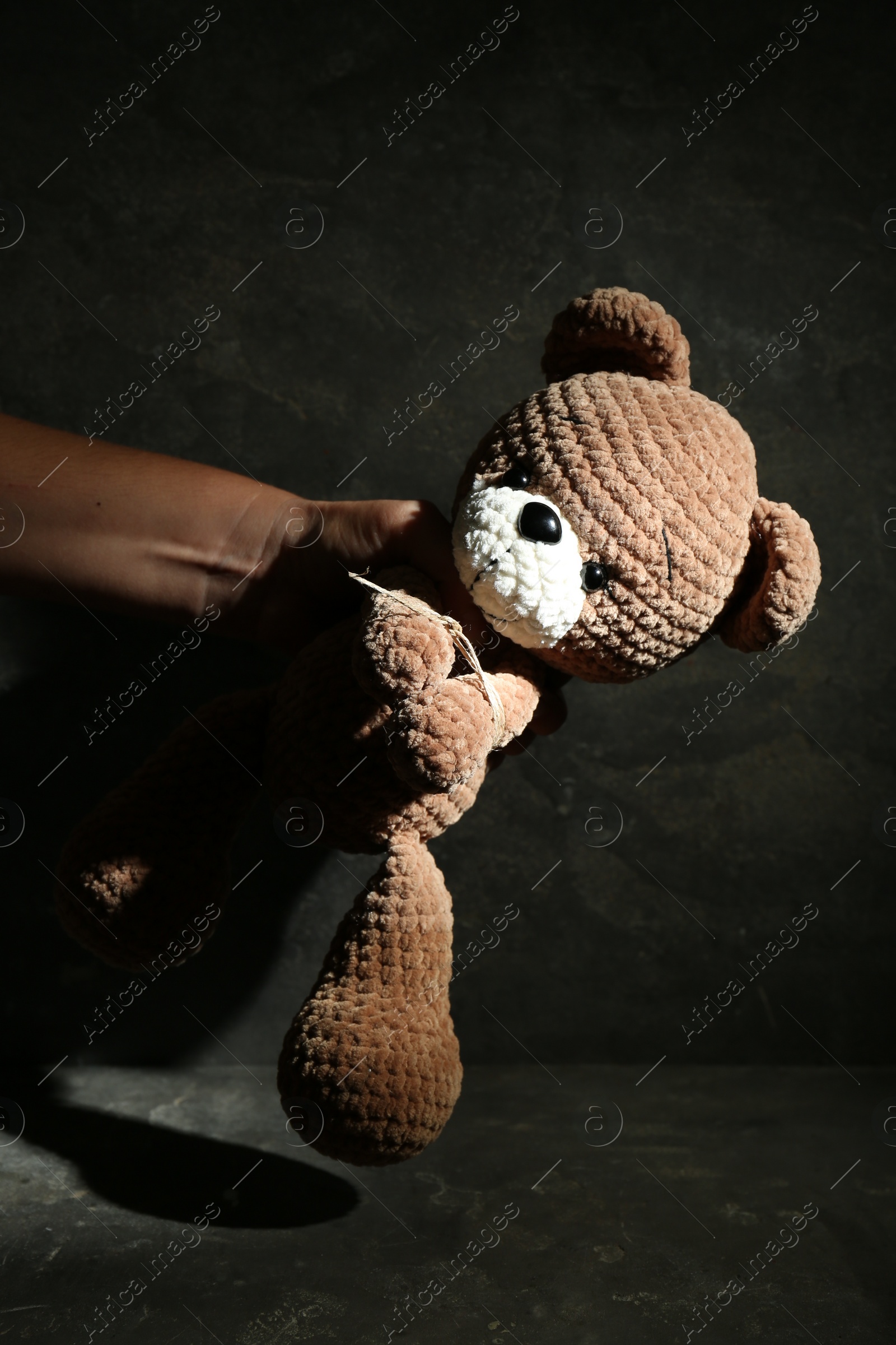 Photo of Stop child abuse. Man punishing toy bear in dark room, closeup