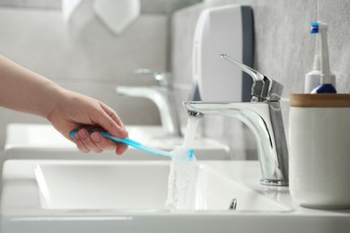 Woman washing plastic toothbrush under flowing water from faucet in bathroom, closeup