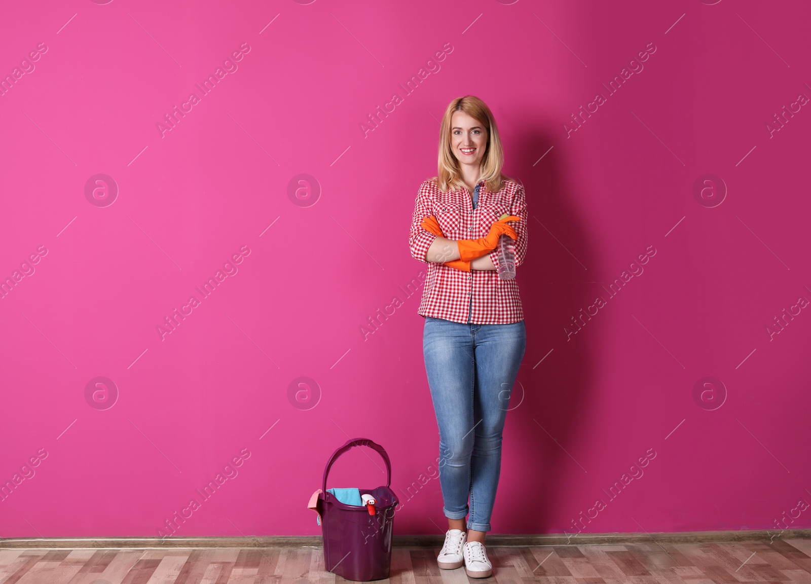 Photo of Woman with cleaning supplies near color wall