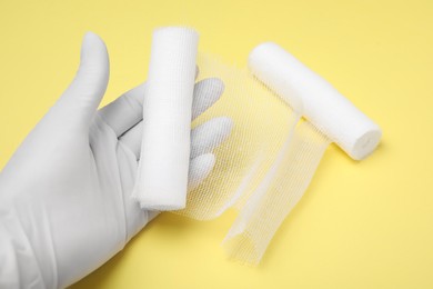 Photo of Doctor holding white bandage rolls on yellow background, closeup
