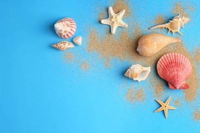 Photo of Beautiful starfishes, shells and sand on blue background, flat lay. Space for text