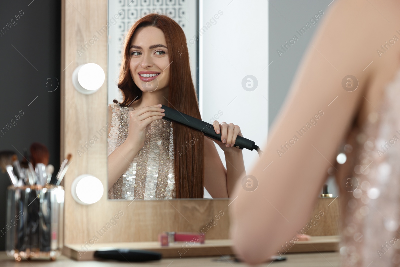 Photo of Beautiful woman using hair iron near mirror in room