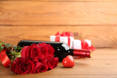 Photo of Beautiful red roses, decorative heart and bottle of wine on wooden table, space for text. Valentine's Day celebration