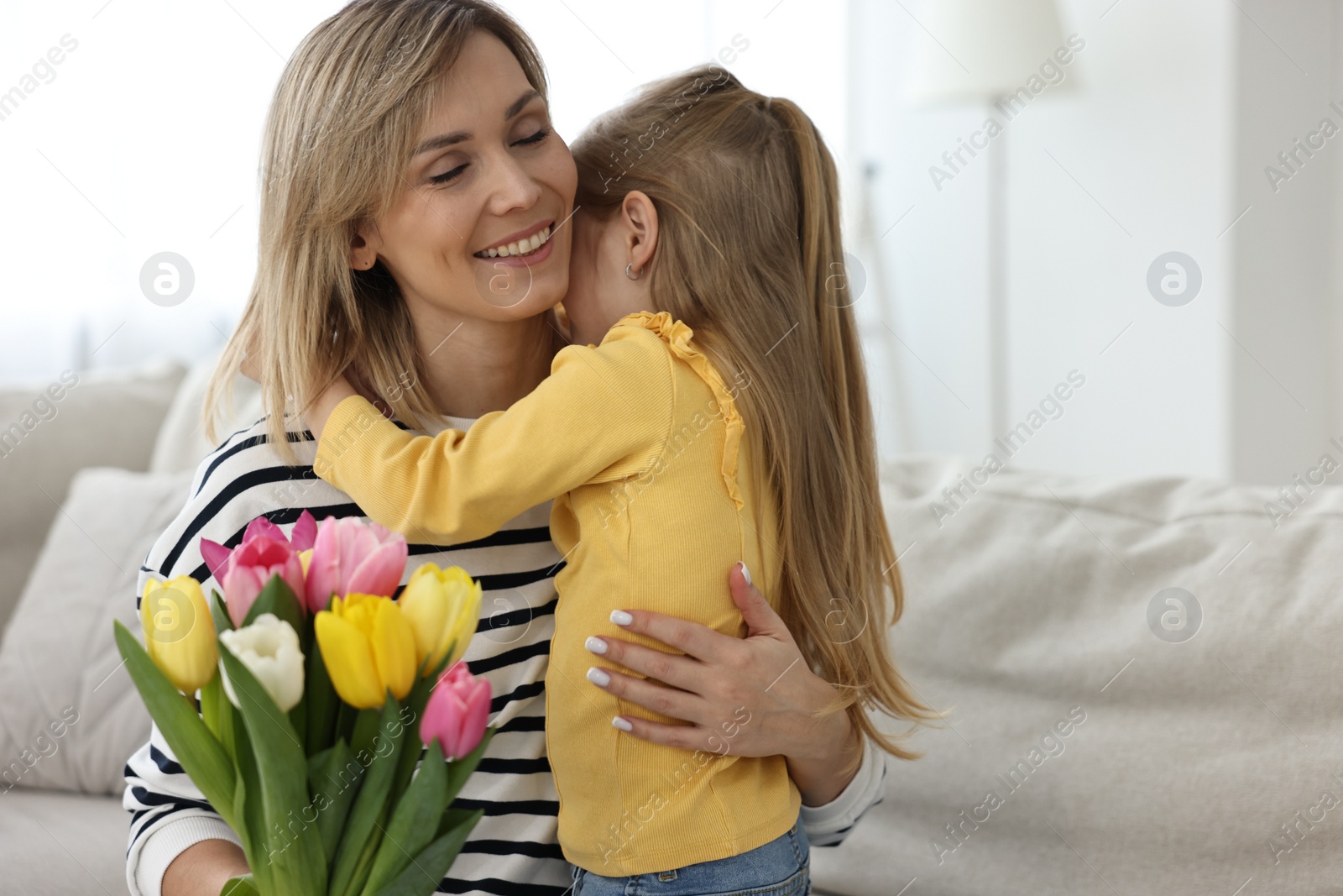 Photo of Little daughter congratulating her mom with Mother`s Day at home, space for text. Woman holding bouquet of beautiful tulips