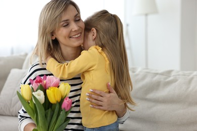 Little daughter congratulating her mom with Mother`s Day at home, space for text. Woman holding bouquet of beautiful tulips