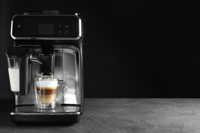 Photo of Modern coffee machine making latte into glass cup on grey table against black background. Space for text