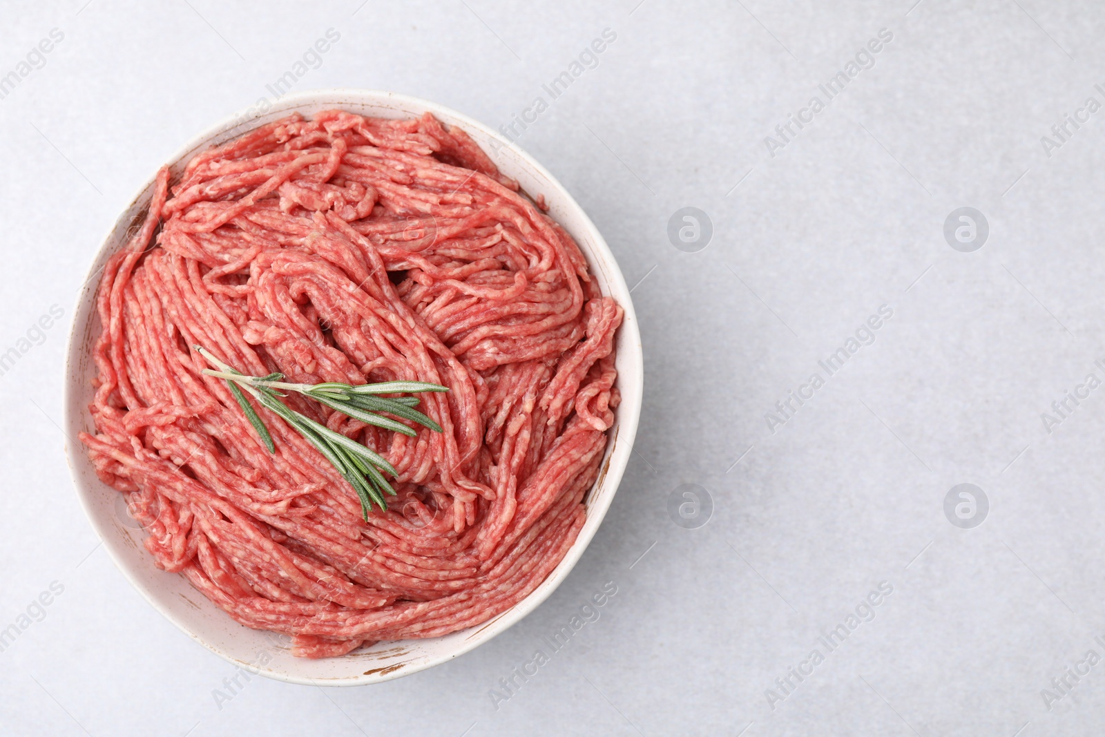 Photo of Fresh raw ground meat and rosemary in bowl on light table, top view. Space for text