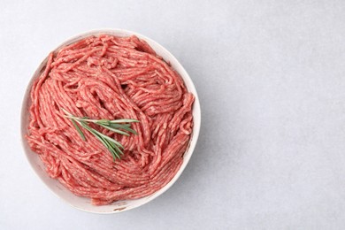 Photo of Fresh raw ground meat and rosemary in bowl on light table, top view. Space for text