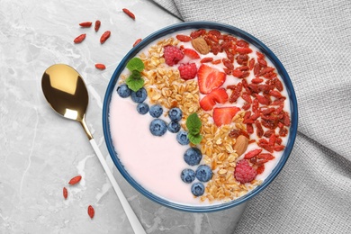 Smoothie bowl with goji berries and spoon on grey table, flat lay